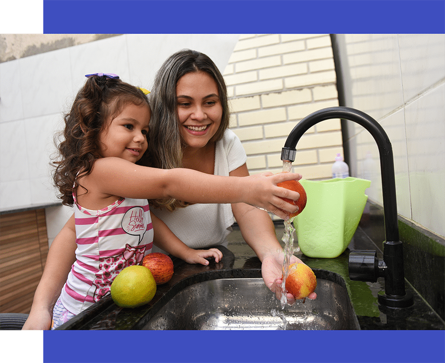 Mãe e filha lavam maçãs e laranjas na torneira de casa
